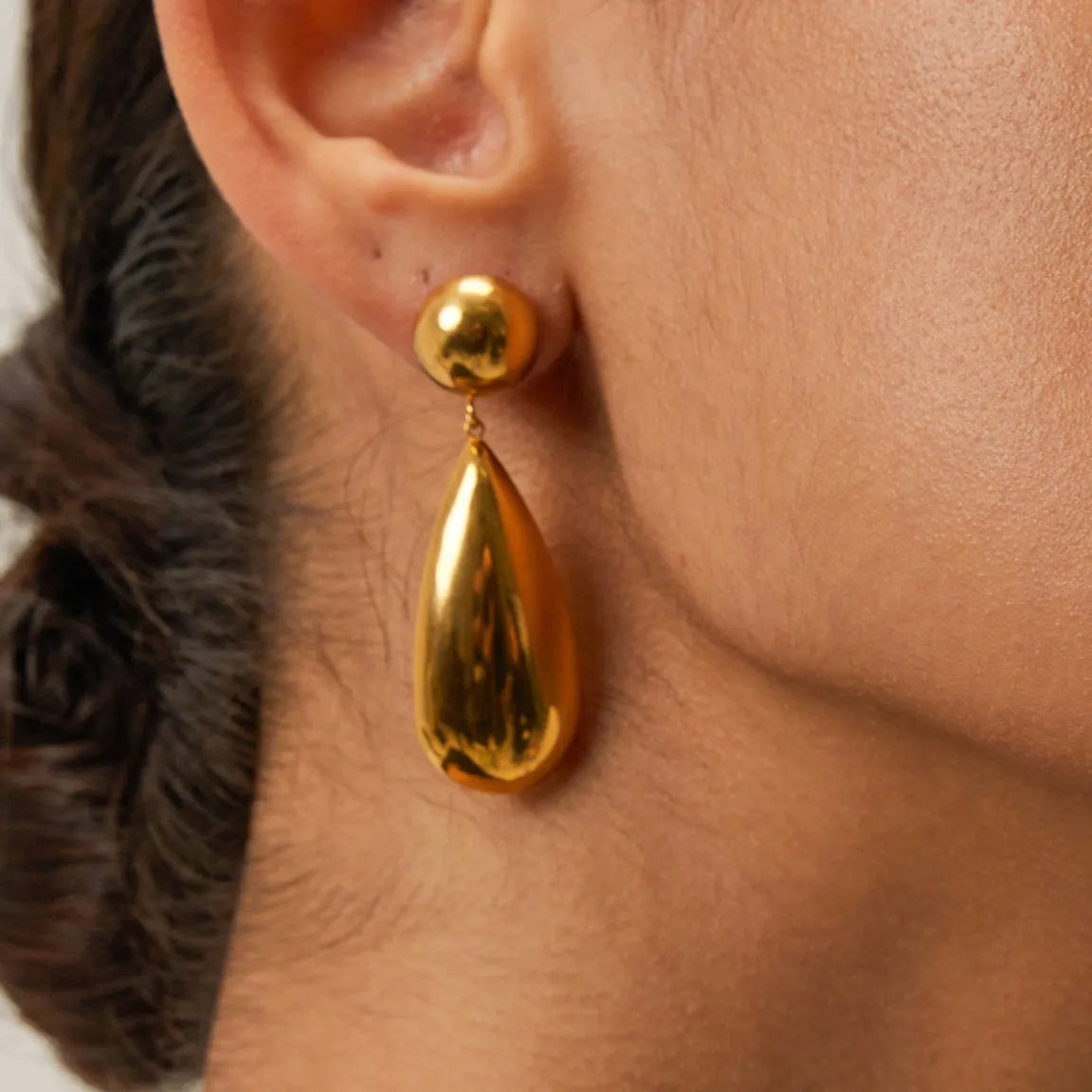 A pair of gold geometric hemisphere earrings with a water droplet pendant design on a white background.