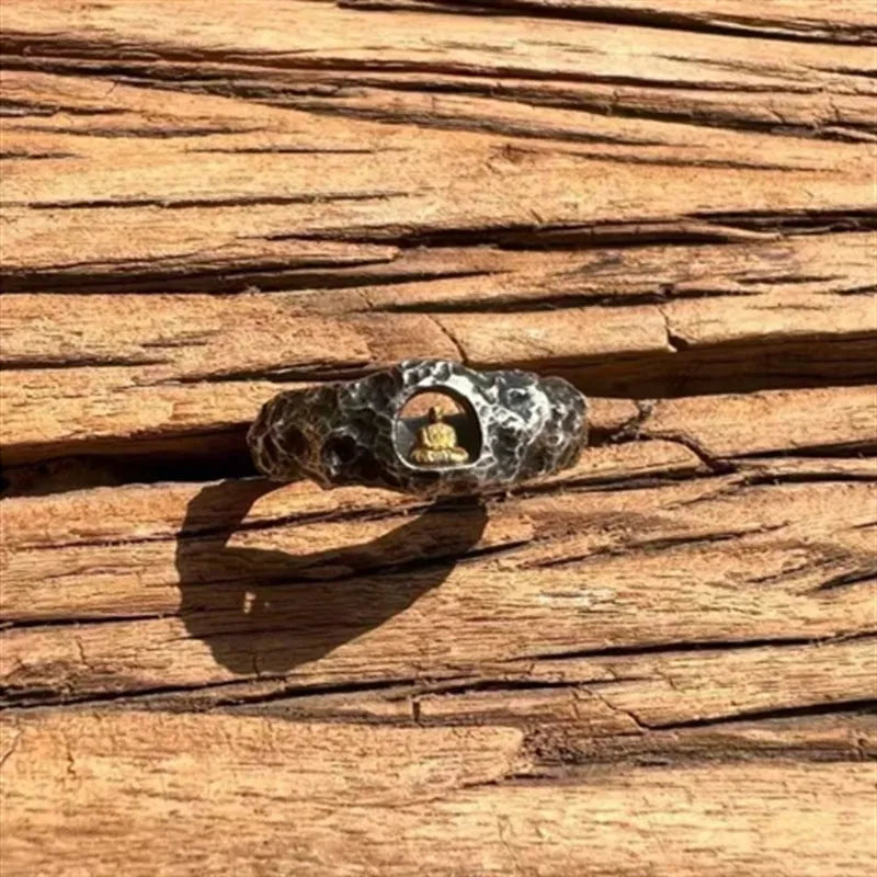 Close-up of a hand-forged copper Buddha ring with a rough rock texture surface.