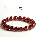 Natural orange red garnet crystal ball bracelet with a gold-toned Ruyi charm on a white background.