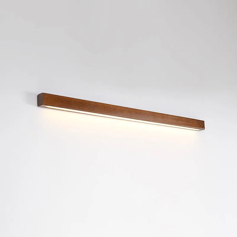 Modern walnut-coloured wood and acrylic log strip wall lamp in three lengths on a white wall.
