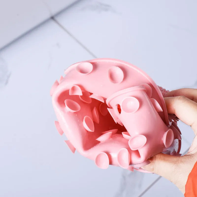 Orange non-slip bath brush with silicone bristles and suction cups on a bathroom floor.