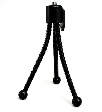 Compact black iron mini tripod with ball head, folded next to an iPhone for scale.