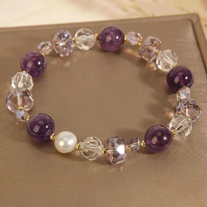 Women's artificial amethyst bracelet with four-leaf clover charm and pearl accents on a wrist.