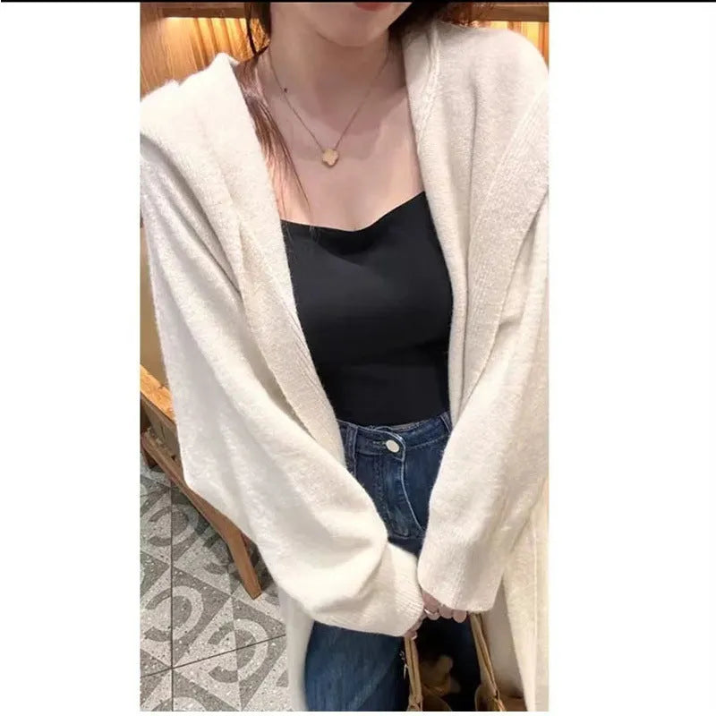 A woman wearing a long, loose-fitting, hooded knitted cardigan in a solid colour, showcasing its below-the-knee length.