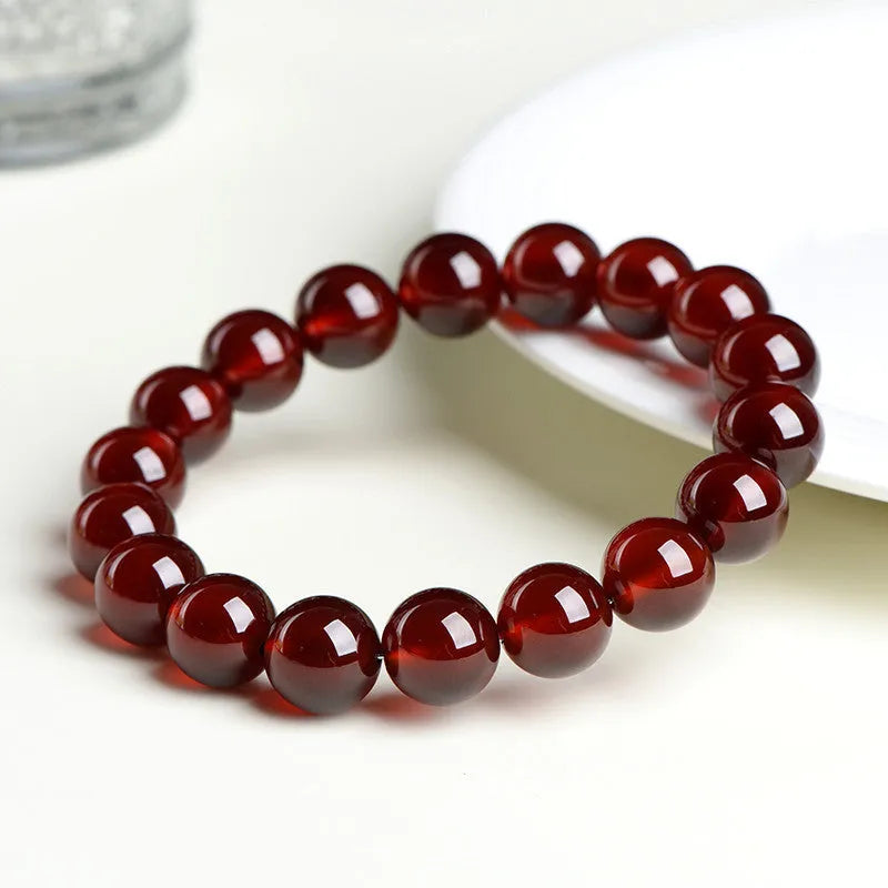 Natural orange red garnet crystal ball bracelet with a gold-toned Ruyi charm on a white background.