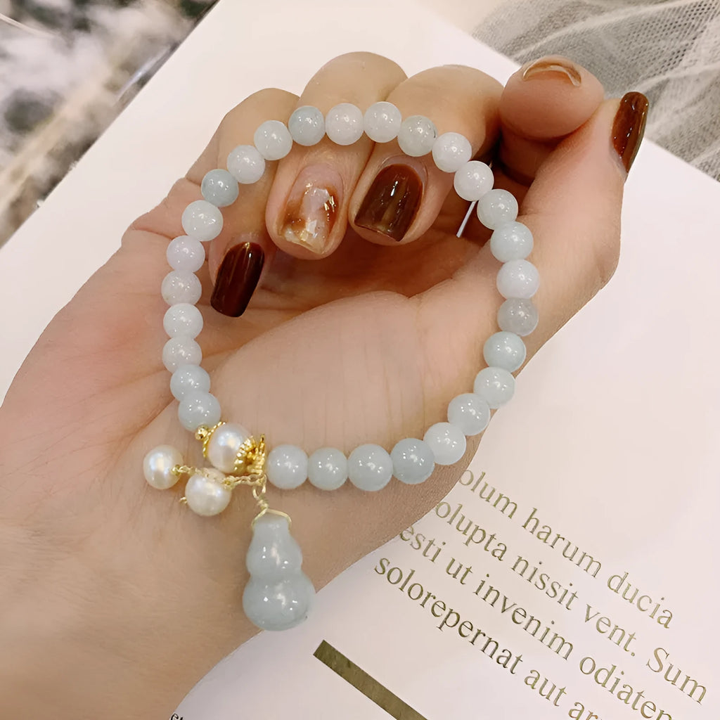 Close-up of a handmade emerald green jade gourd charm bracelet with a pearl detail on an adjustable cord.