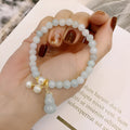 Close-up of a handmade emerald green jade gourd charm bracelet with a pearl detail on an adjustable cord.
