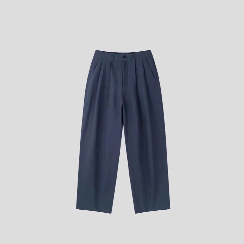 Men's apricot coloured wide-leg cotton linen trousers with a mid waist and zip fly on a neutral background.