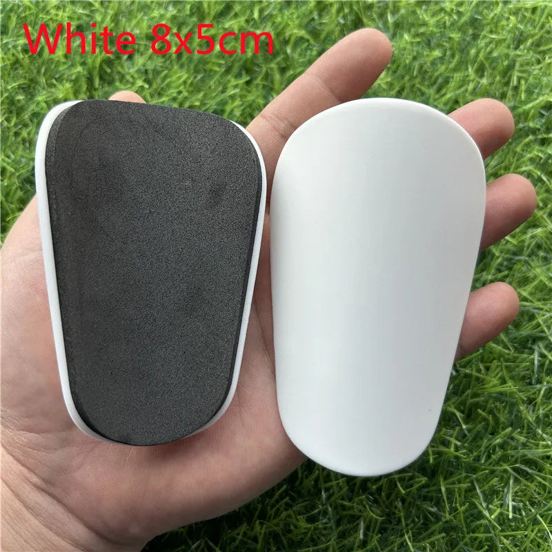 Extra small mini plastic football shin guards in black and white, shown at 8cm by 5cm size.
