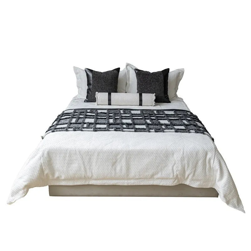 Modern gray and white plaid bed runner blanket with matching pillowcase and round leather-look pillow on a bed.