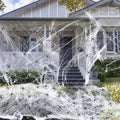 White cotton Halloween spider web decoration draped on a surface with scattered plastic spiders.