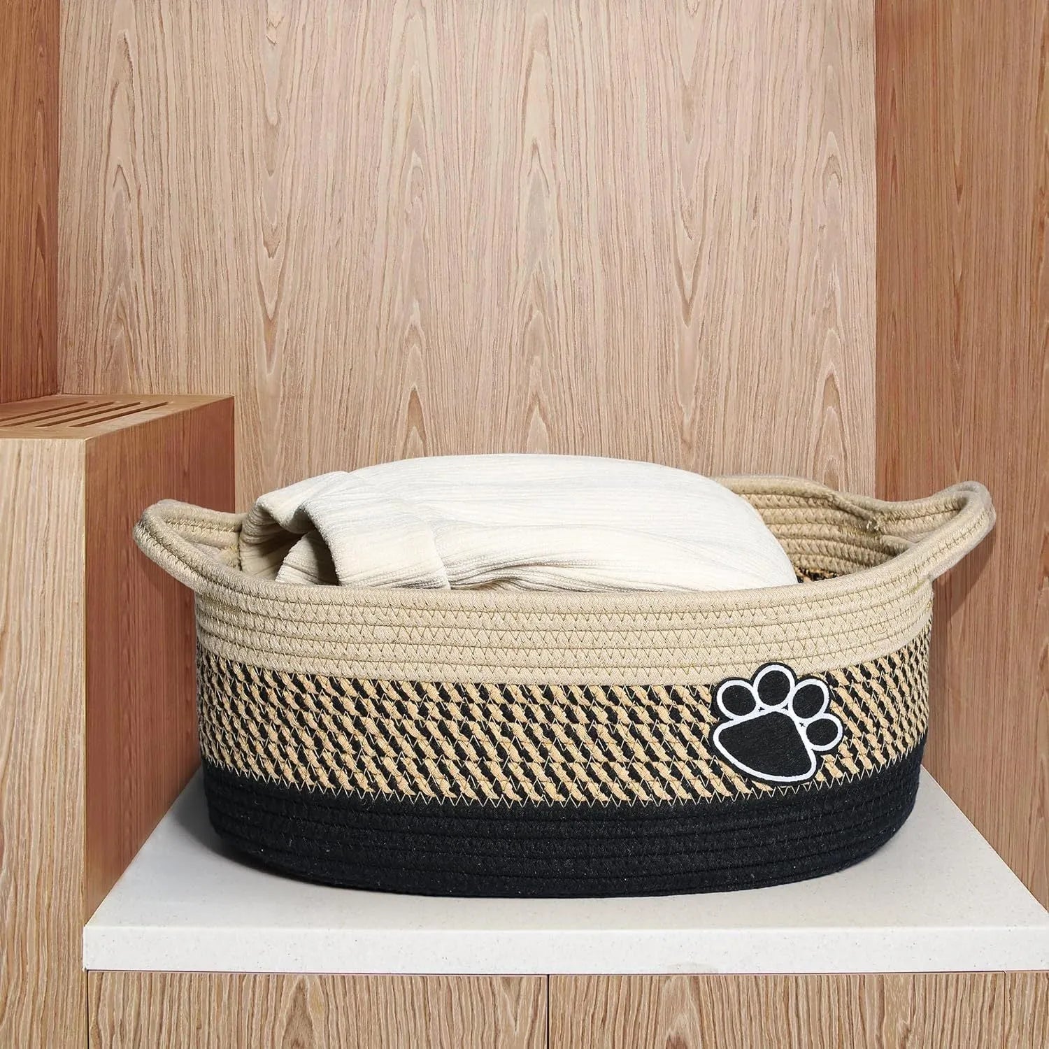 Light beige handmade cotton rope woven storage basket with handle on a wooden base.