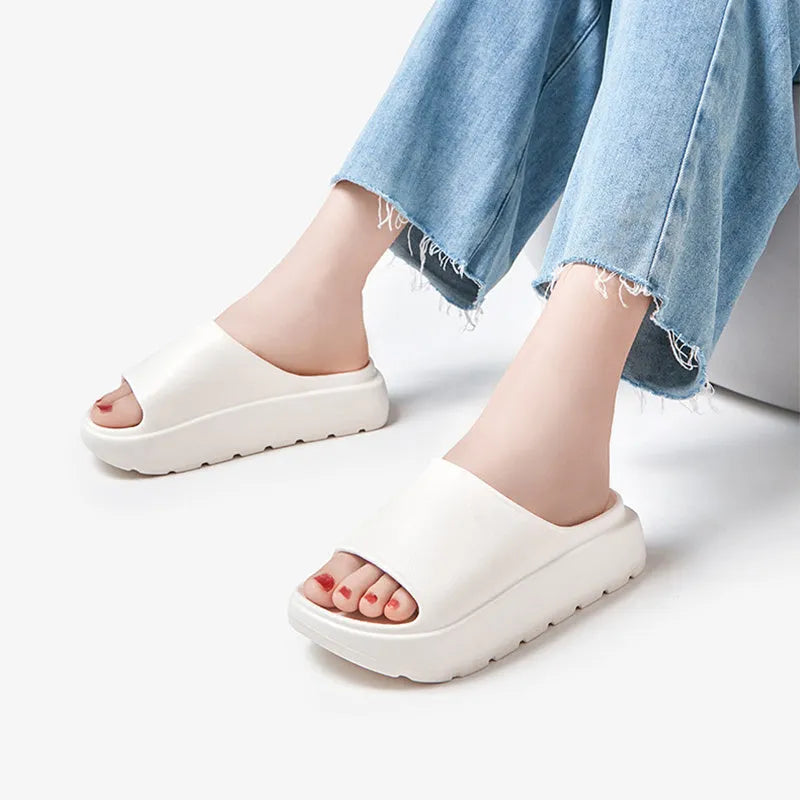 Women's beige thick-soled EVA beach slippers with fish mouth design on a wooden floor.