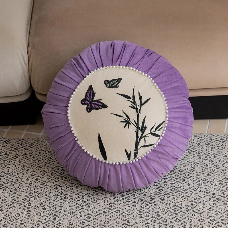 Square beige cushion with butterfly embroidery on a sofa, showing purple and black colour options.