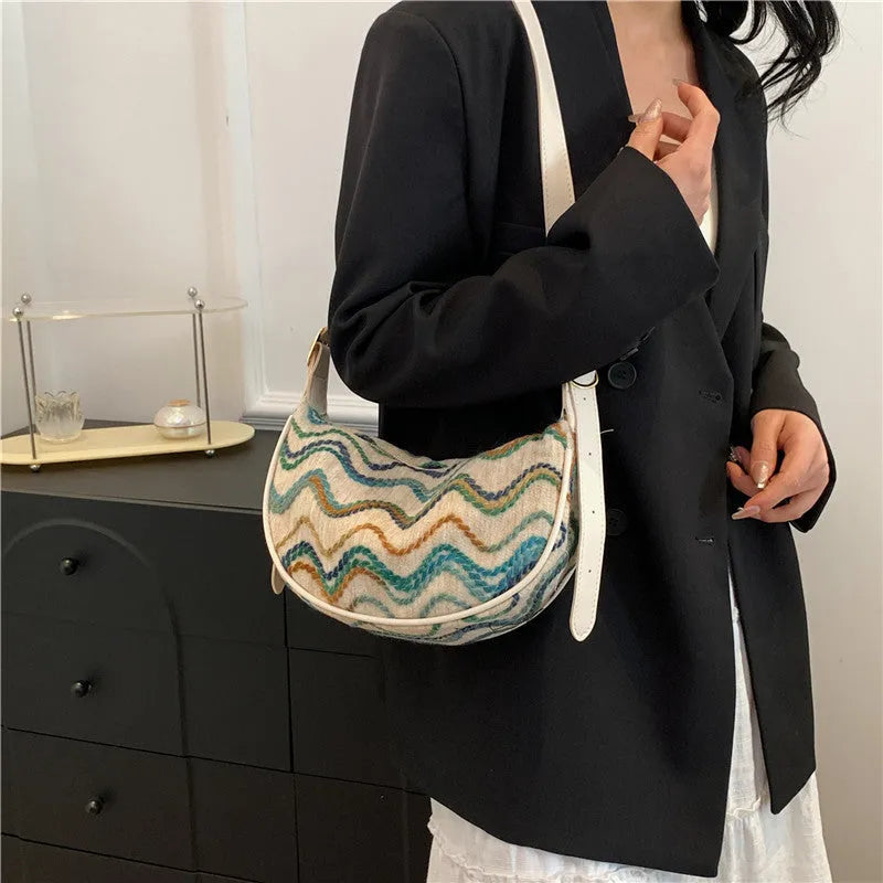 Women's straw woven crossbody bag showing knitted texture and single shoulder strap, shown in corrugated black colour.
