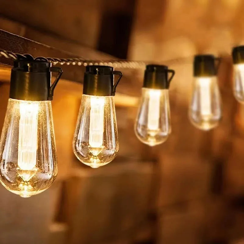 Retro long bulb outdoor string lights in a garden setting, showing solar panel, battery box, and USB power options.