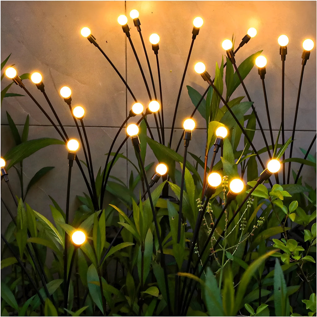 Solar-powered LED firefly garden stake light with stainless steel ground plug illuminated at dusk.