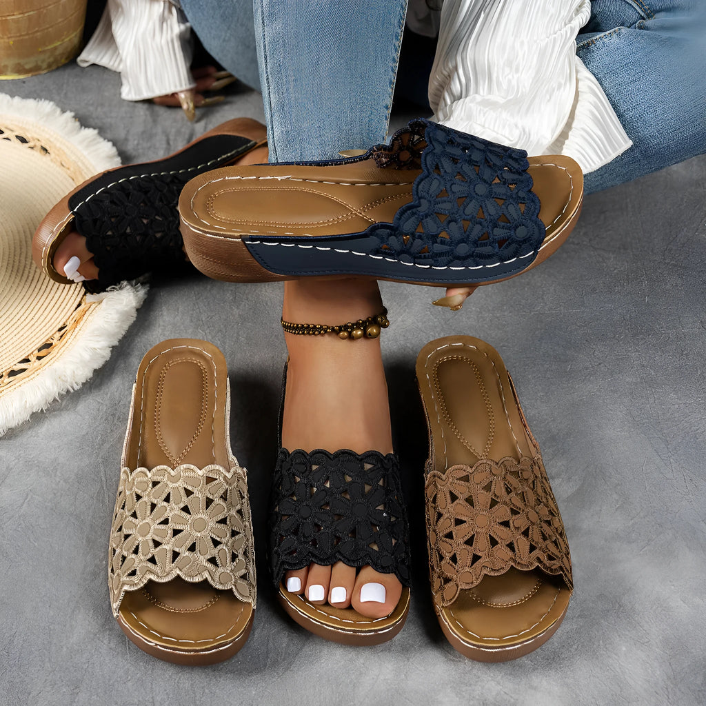Women's black beach slippers with a flower cutout design on the upper and a wedge-style rubber sole.