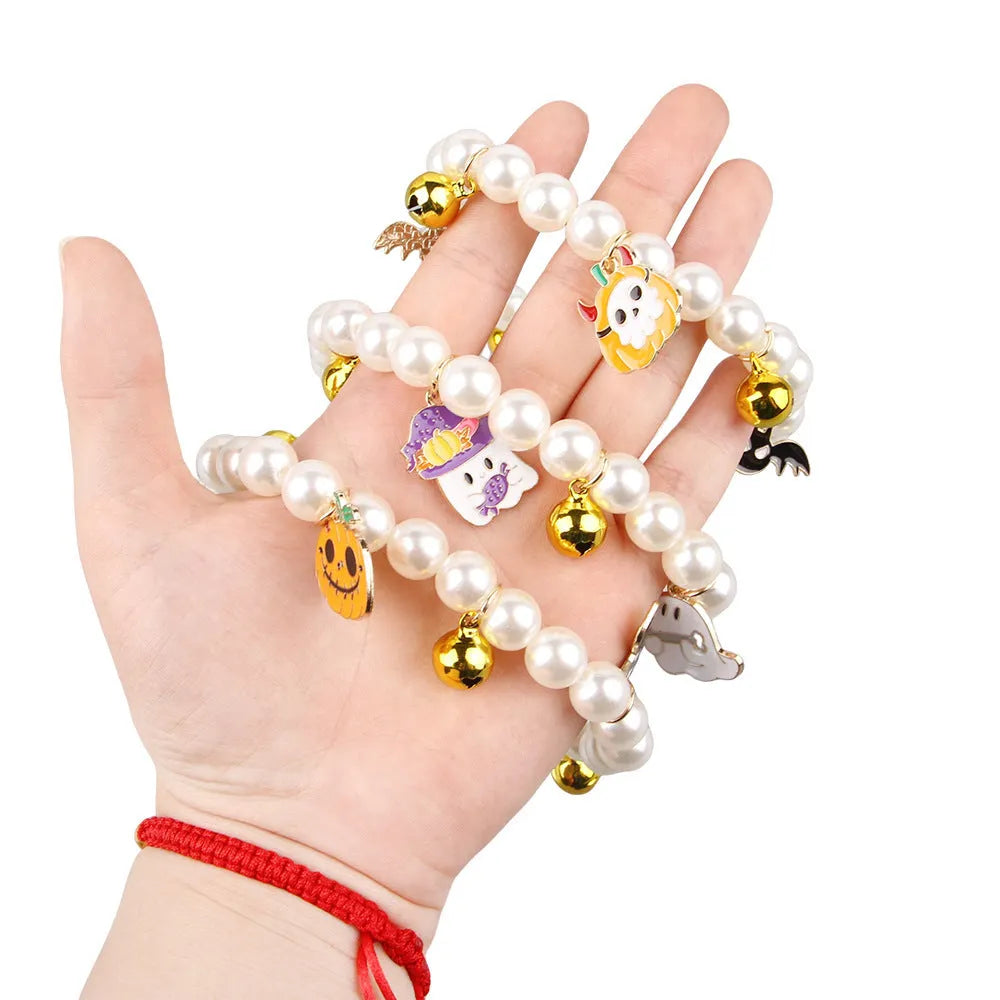 Set of three pet necklaces: a pearl strand, a Halloween cat collar, and a dog bell ornament on a table.