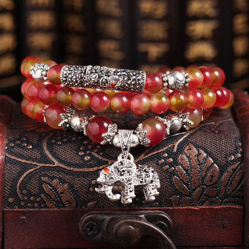 A handmade bracelet with geometrically cut watermelon crystal beads and a red Chinese knot closure on a white background.