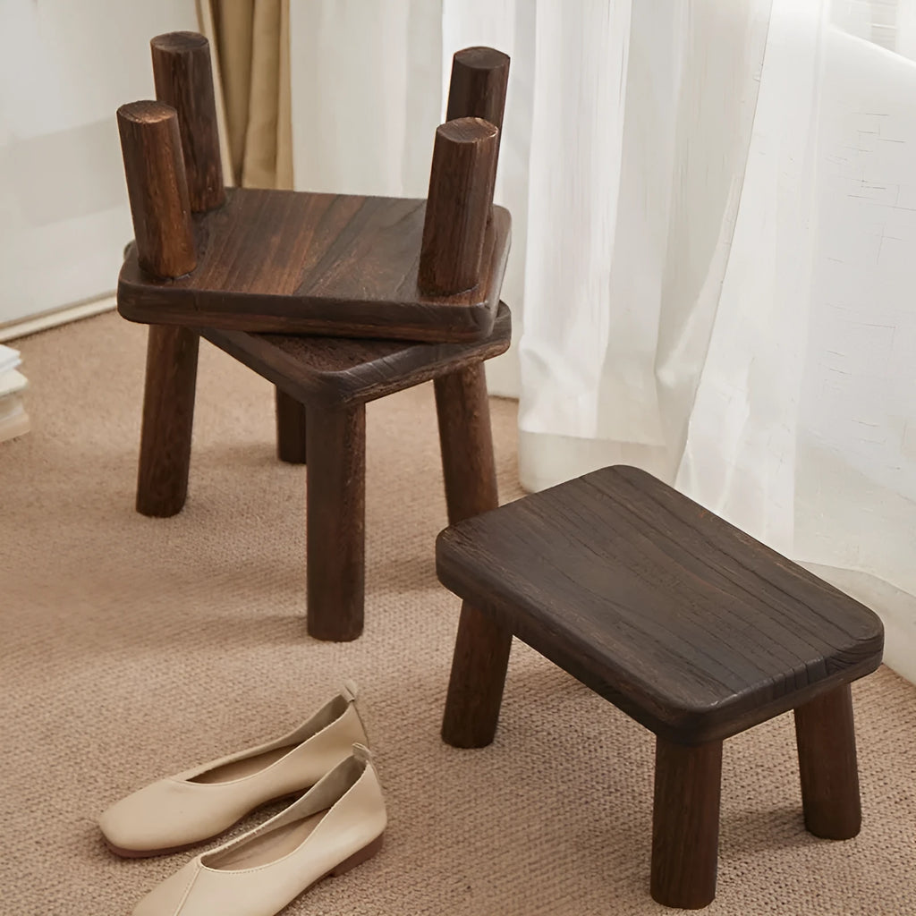 A solid wood stool with a distressed finish, used for changing shoes in a living room.