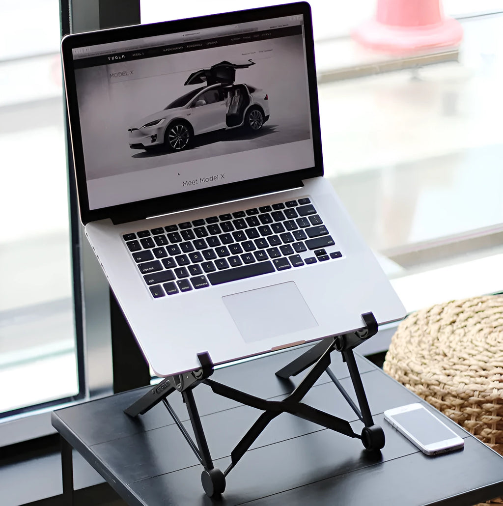 Black folding portable laptop stand with reinforced nylon construction shown unfolded beside laptop