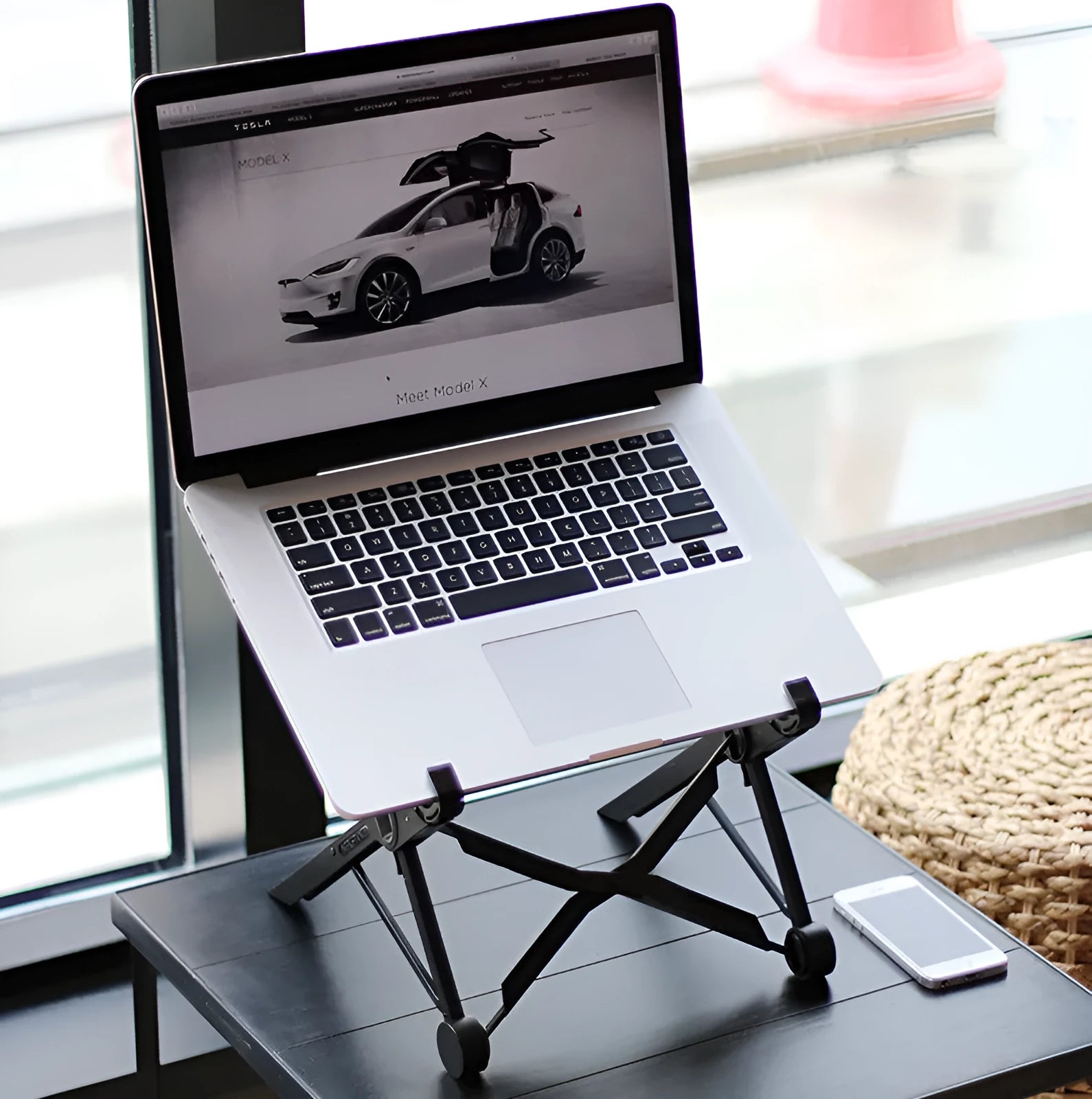 Black folding portable laptop stand with reinforced nylon construction shown unfolded beside laptop