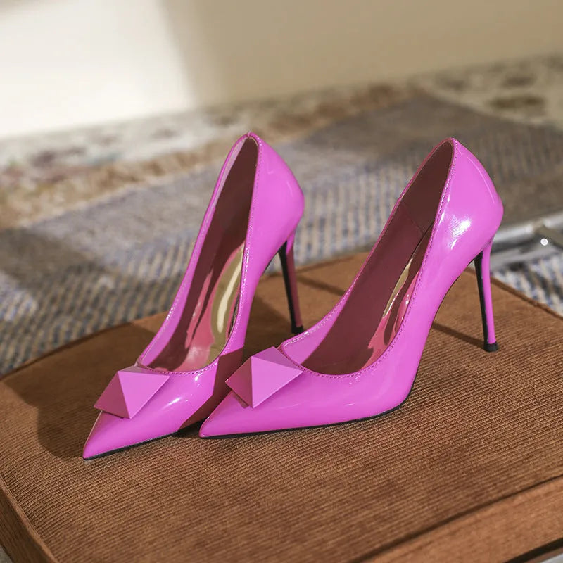 Pink patent leather women's stiletto heels with pointed toe, rivet buckle, and low-cut vamp on a white background.