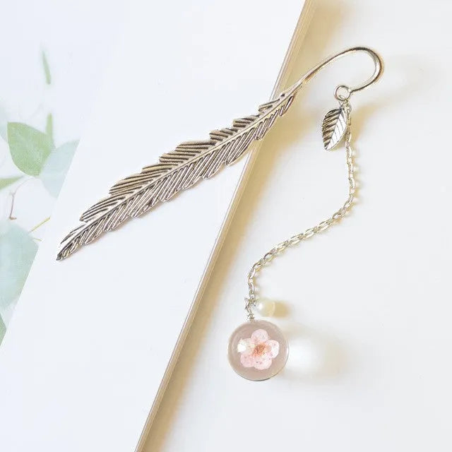 Close-up of a metal alloy bookmark with real dried pink flowers sealed inside, on an open book.