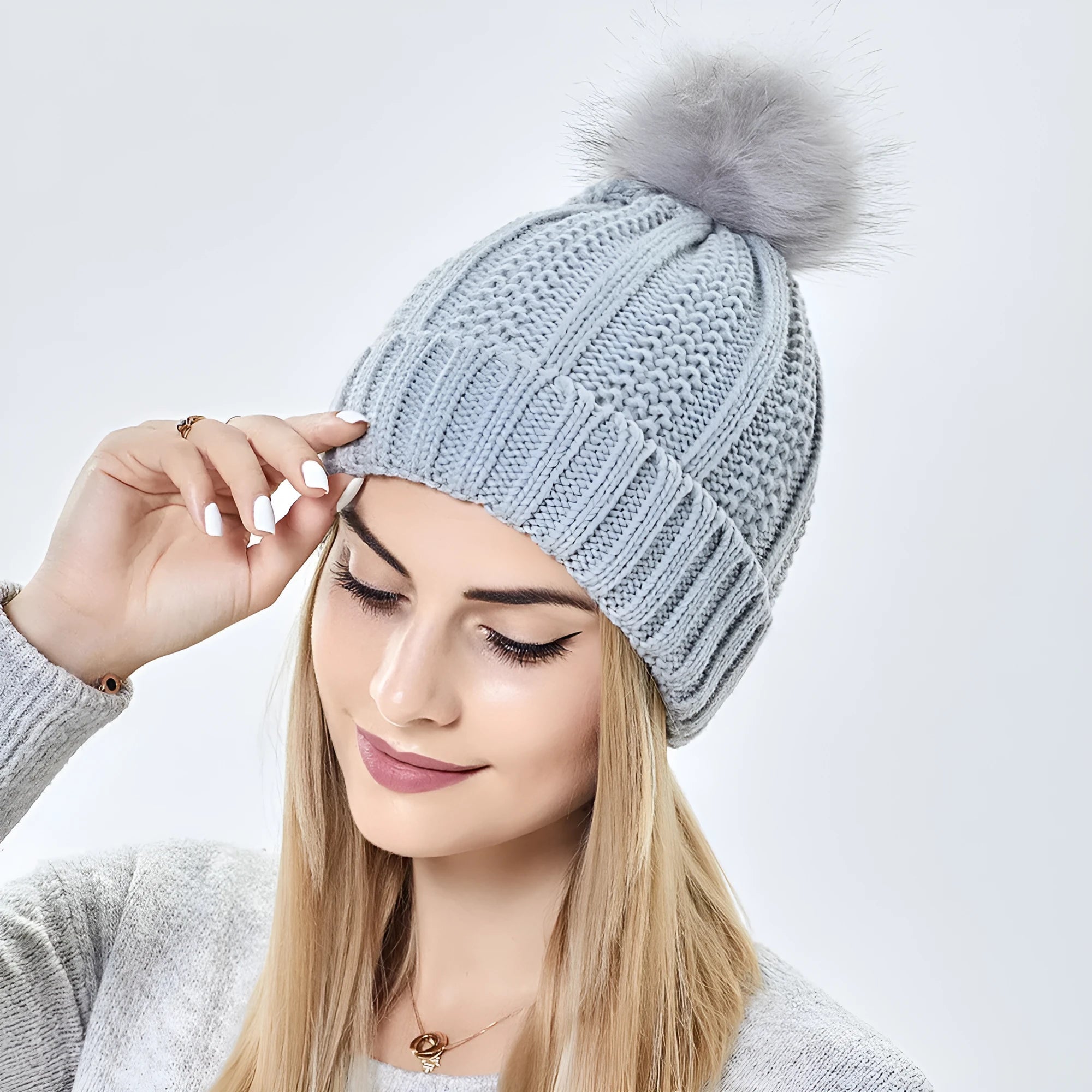 Women's black knit beanie hat with a white faux fur pom pom and visible satin lining.