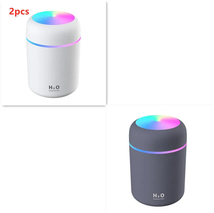 Pink USB mini humidifier with LED lights on wooden desk beside laptop
