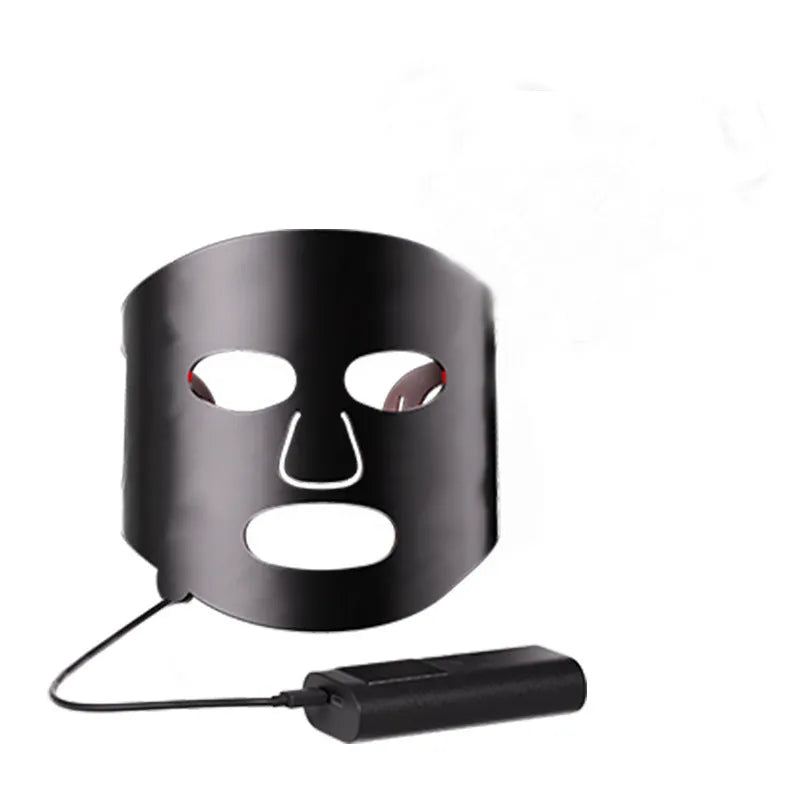 Black and white LED phototherapy face mask with controller and strap on a table.