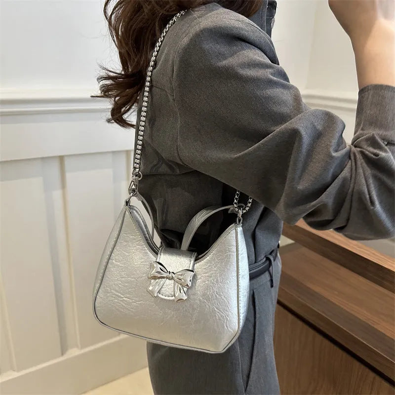 Bow underarm bag in textured PU with one-shoulder strap, dumpling shape and sandwich pocket, shown in black, pink, silver or white