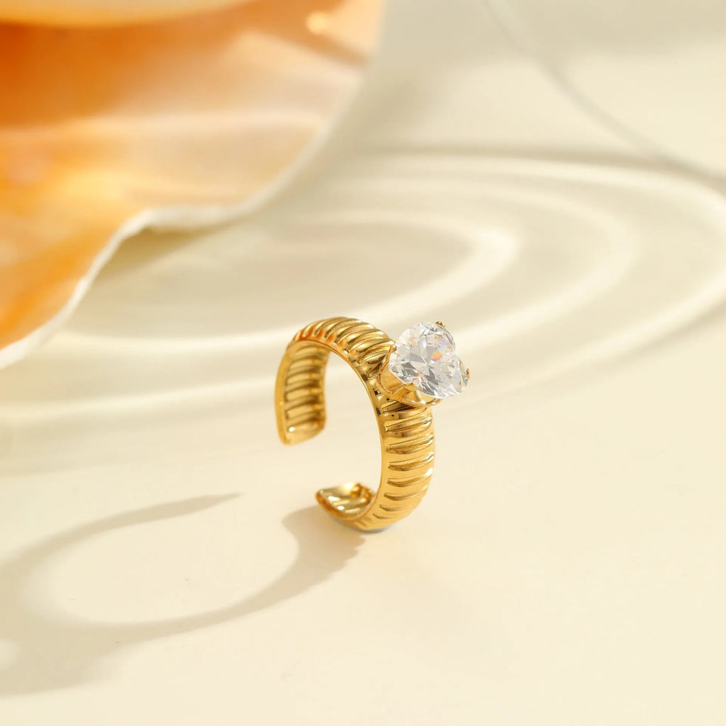 Geometric gold-coloured stainless steel ring with open mouth design on a plain background
