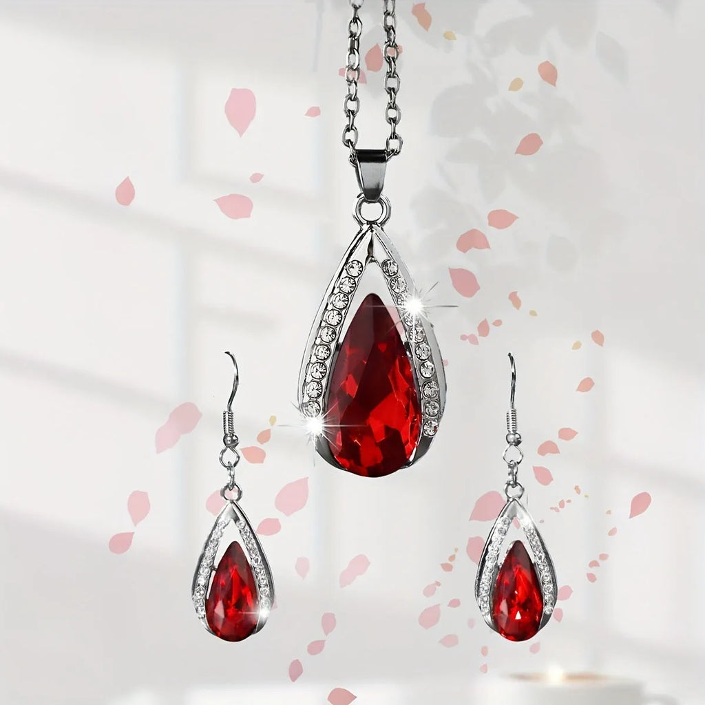 Close-up of a black alloy teardrop pendant necklace and matching drop earrings with glass details on a plain background.