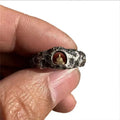 Close-up of a hand-forged copper Buddha ring with a rough rock texture surface.