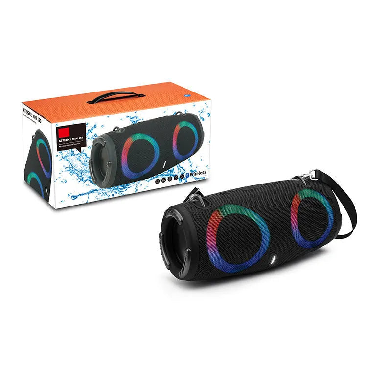 Cylindrical War Drum Bluetooth speaker with glowing RGB lights, a black metal grille, and a carrying strap on a wooden table.