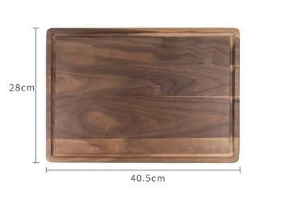 Black walnut wood chopping board with side handle and circular serving groove on a kitchen counter.