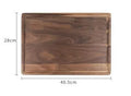 Black walnut wood chopping board with side handle and circular serving groove on a kitchen counter.