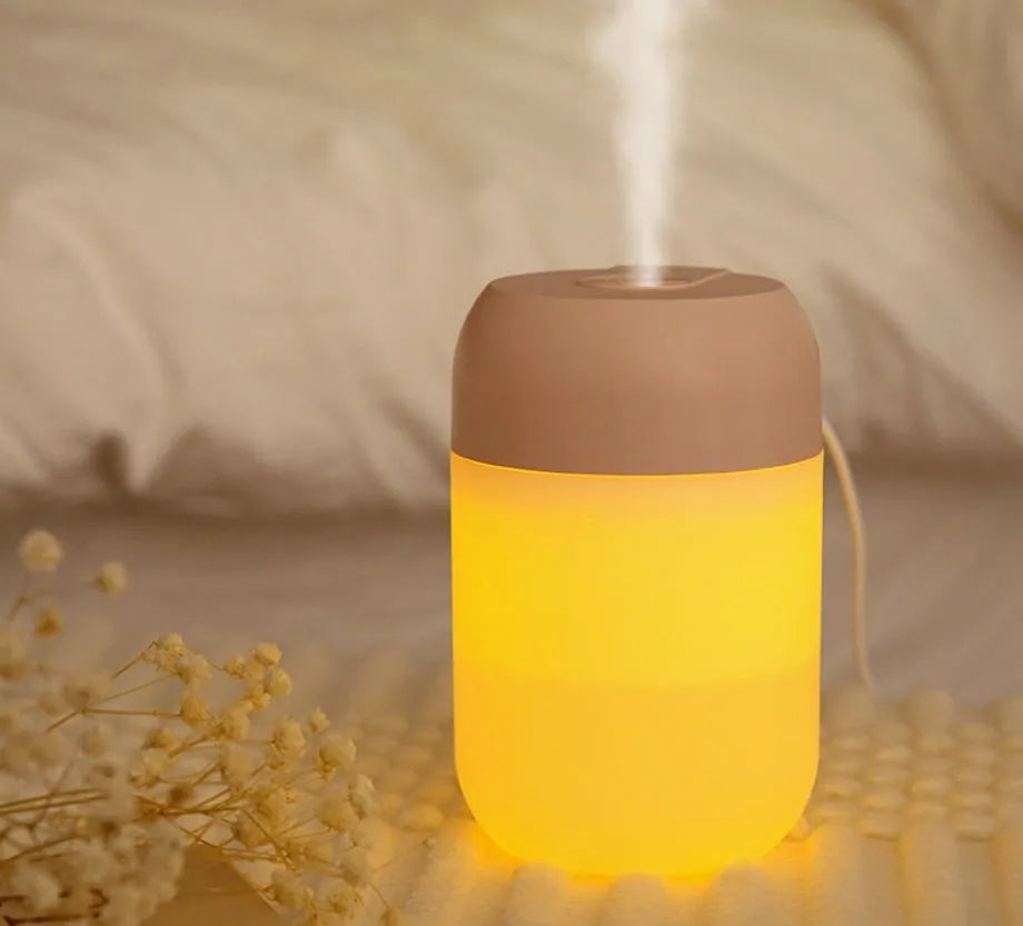 White cylindrical mini humidifier with USB cable and aromatherapy tray on a wooden desk.