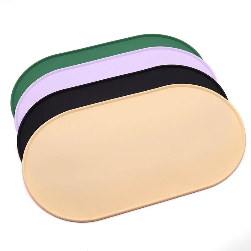 Green silicone cat feeding mat with raised edge containing a food bowl and scattered kibble on a kitchen floor.