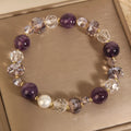 Women's artificial amethyst bracelet with four-leaf clover charm and pearl accents on a wrist.