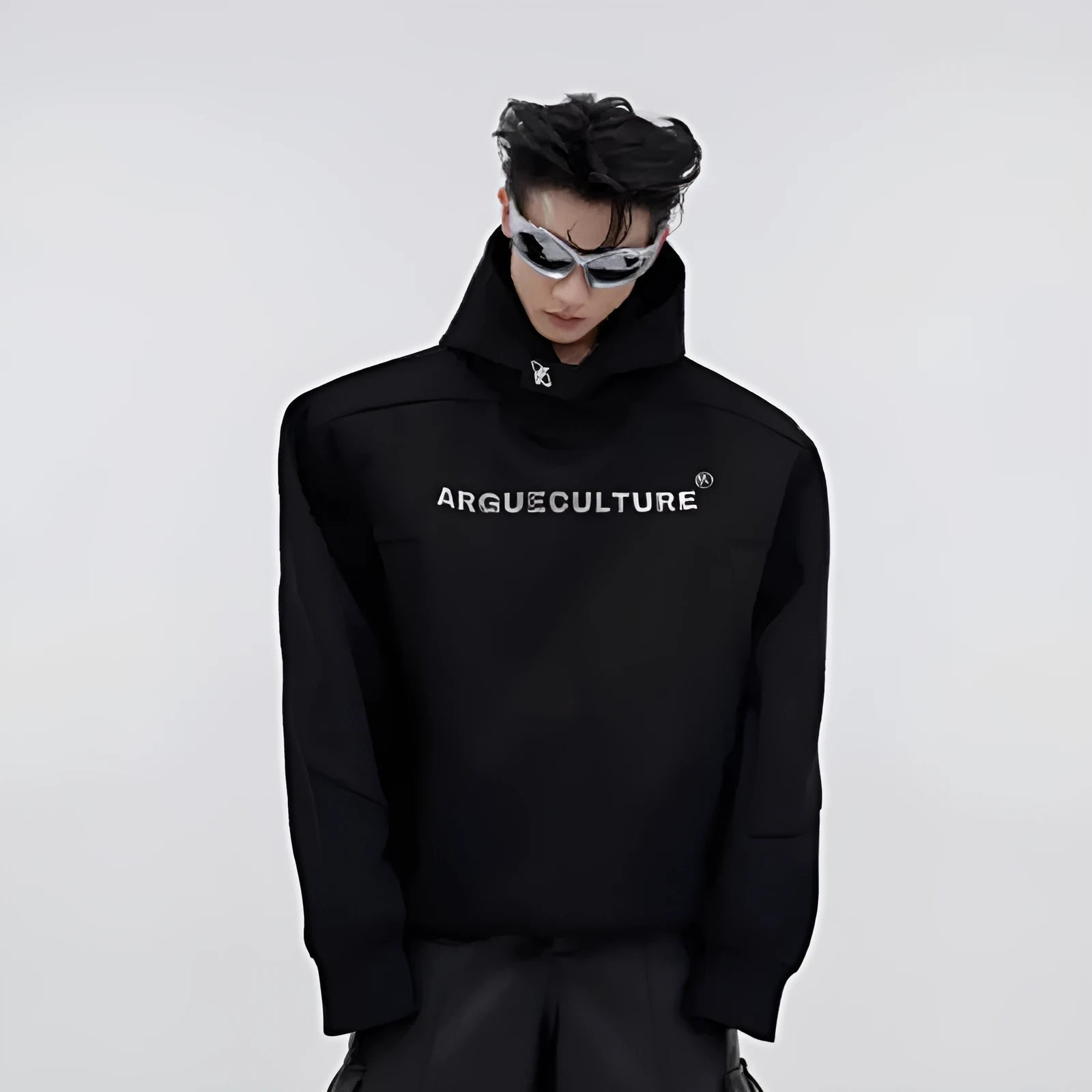 Man wearing a loose black hooded sweater with metallic 3D printed design and structured shoulder pads.