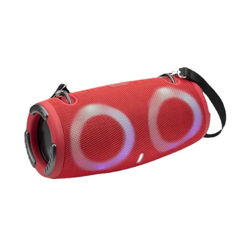 Cylindrical War Drum Bluetooth speaker with glowing RGB lights, a black metal grille, and a carrying strap on a wooden table.