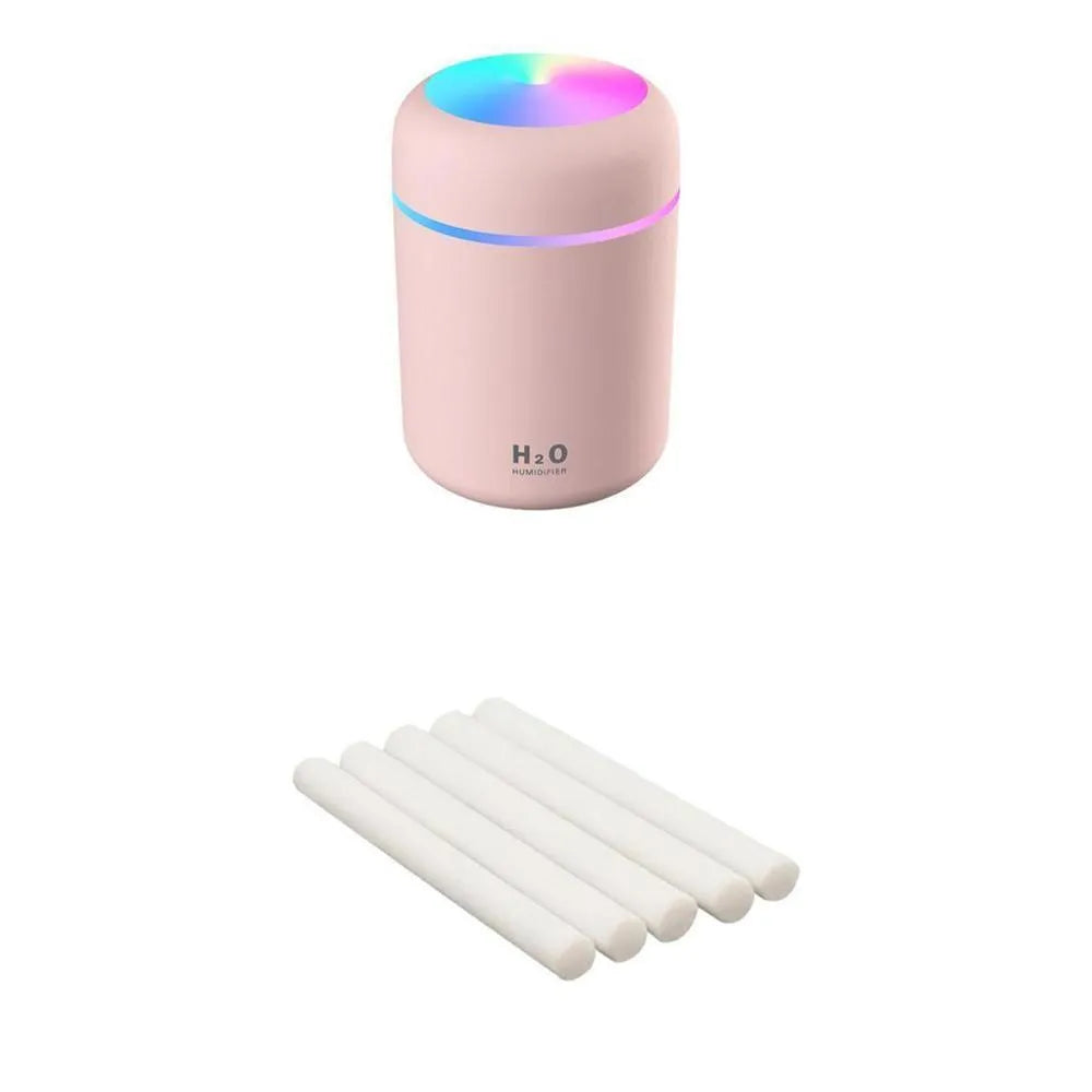 Pink USB mini humidifier with LED lights on wooden desk beside laptop