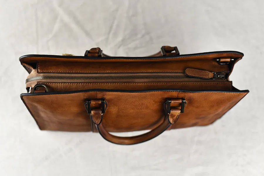 Men's brown leather horizontal business handbag with zipper, shown next to a 14-inch laptop for scale.