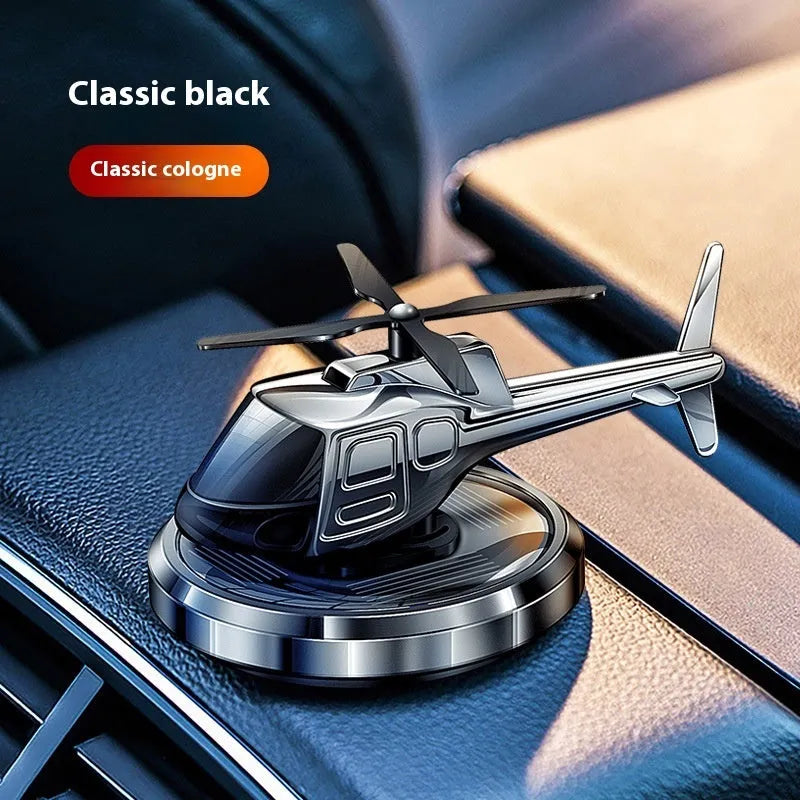 Silver metal solar-powered helicopter car air freshener rotating on a car dashboard.