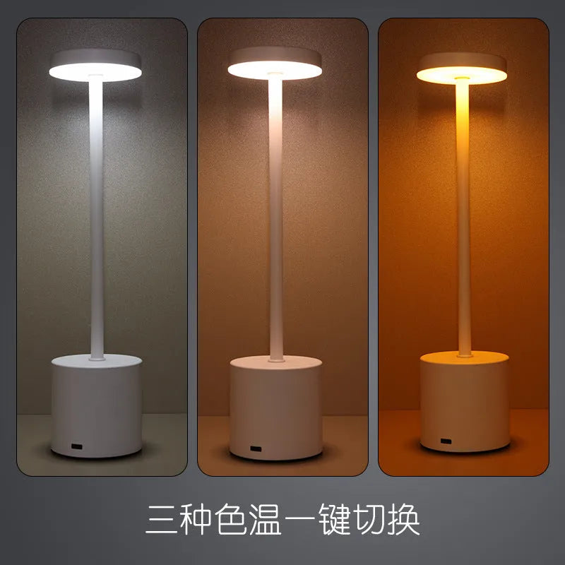 Modern minimalist iron table lamp with silver finish, I-shaped silhouette, emitting warm ambient light on a bedside table