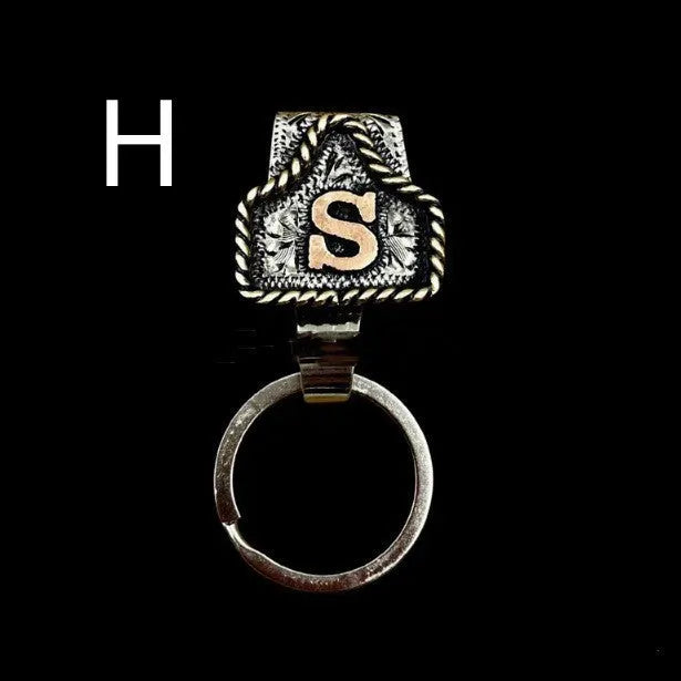 Handmade metal cow tag belt keychain showing one of 26 colour options, each marked with a different alphabet letter.