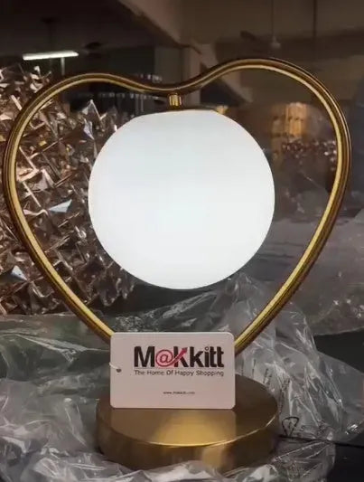 Red heart shaped plastic lamp with glowing LED light and USB cable on a table.